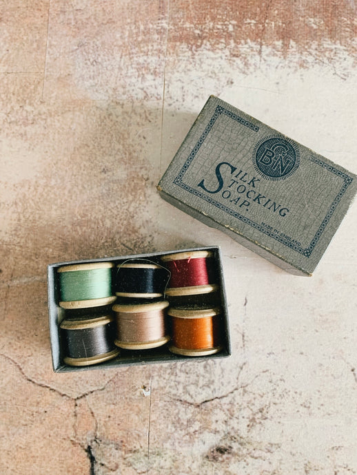 A vintage soap box filled with six vintage thread spools